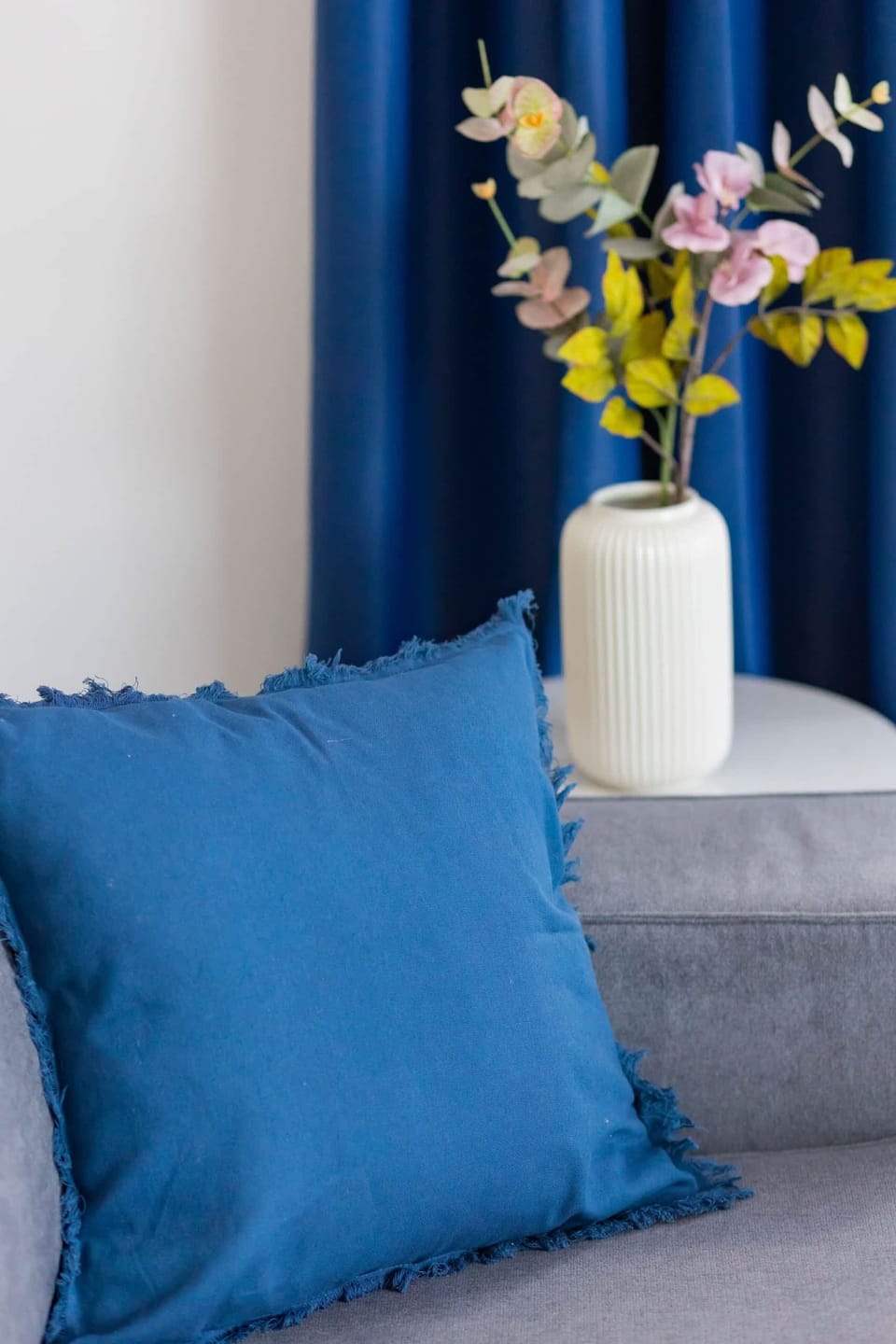 A close-up of a vase of flowers placed on a side table next to a vibrant blue cushion.
