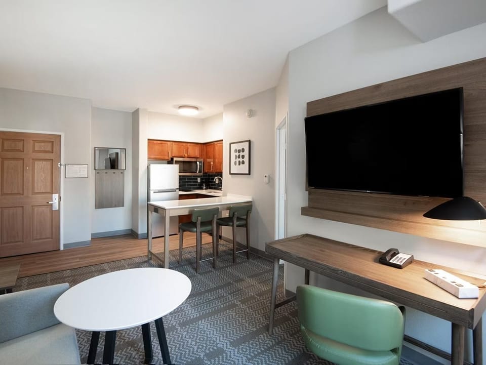 Living area with sofa bed, flat-screen TV, work desk, and kitchen visible in the background