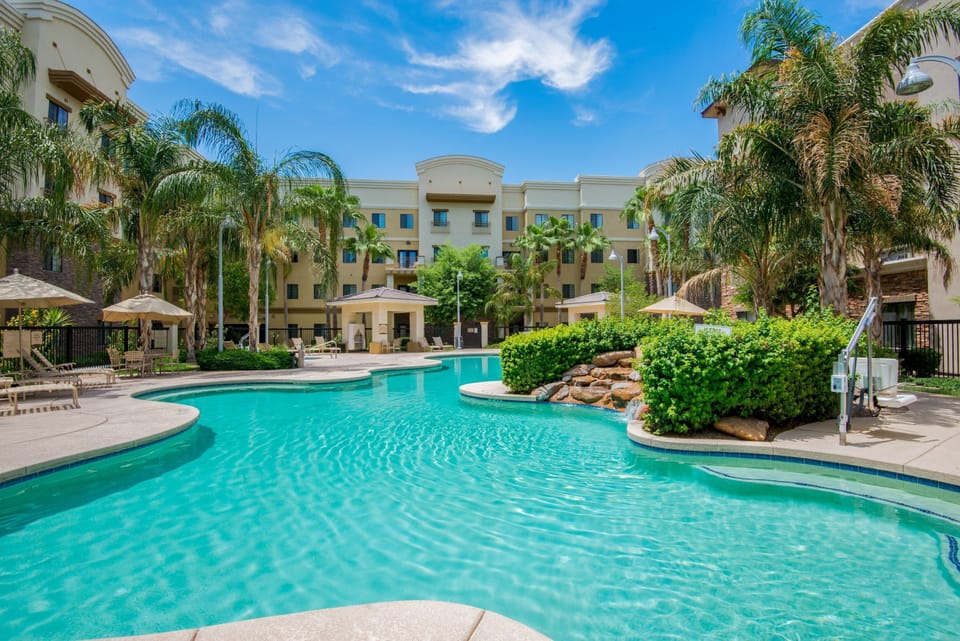 Outdoor pool surrounded by palm trees and lounge chairs.