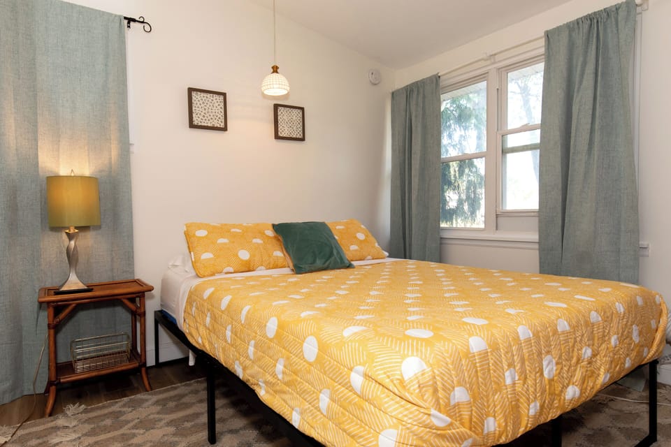 Sink into your comfortable bed with cheerful yellow bedding while gentle light filters through sage curtains, creating a peaceful retreat.
