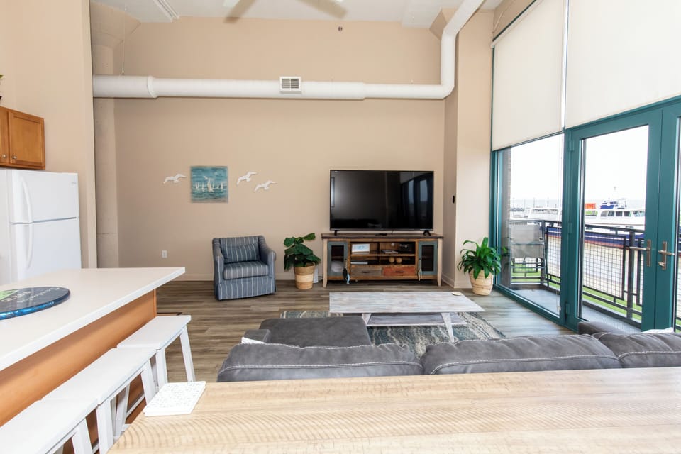 Relax in your spacious living area with harbor views through floor-to-ceiling windows, complete with modern kitchen and cozy seating.