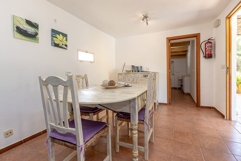 Bright dining room with a rustic wooden table, classic chairs and access to the interior hallway, offering a cozy space for family meals.