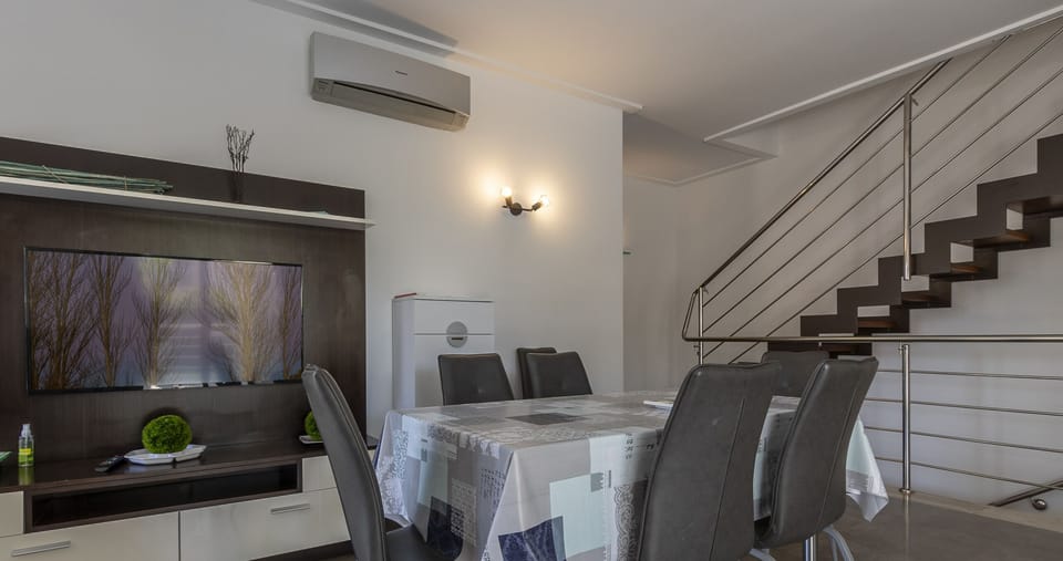 Modern indoor dining area at Villa Albufera, featuring a spacious table, contemporary chairs, TV and a designer staircase, a bright and comfortable space for family stays in Mallorca.