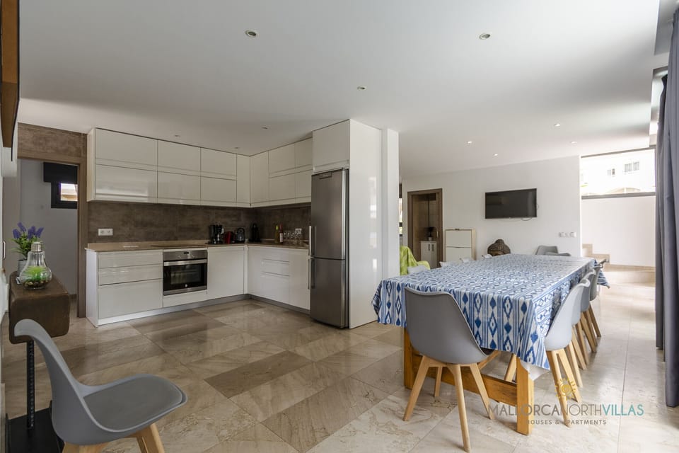 Bright open-plan living space featuring a fully equipped modern kitchen and integrated dining area, perfect for enjoying meals together in a spacious and functional setting at Villa Iola in Playa de Muro.