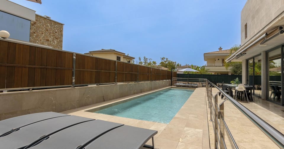 Long private swimming pool at Villa Iola in Playa de Muro, surrounded by a spacious natural stone terrace with sun loungers, stainless steel railings and direct access to the interior of the villa.
