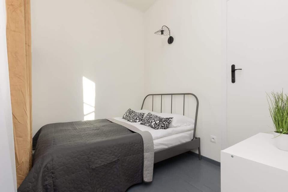 A similar bedroom perspective, showing the bed, a white nightstand, and a wall lamp.

