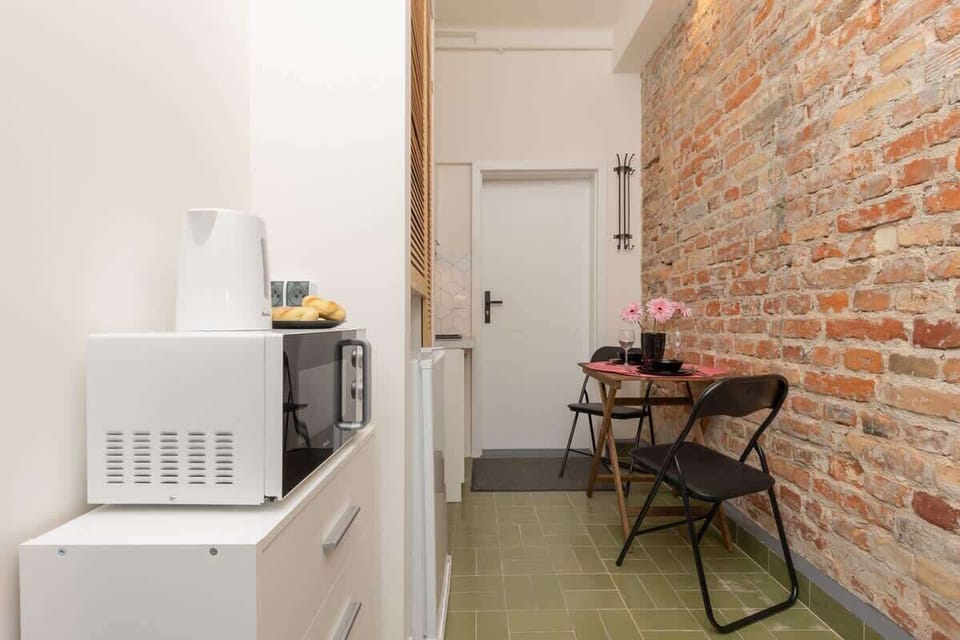A kitchenette area with a microwave, white cabinets, and an exposed brick wall.


