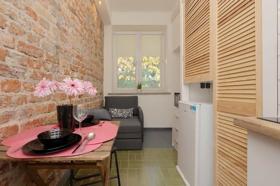 A small dining area with an exposed brick wall, a round table, and a kitchenette in the background.

