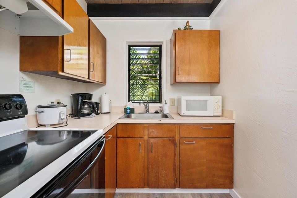 Your fully equipped kitchen features warm wood cabinetry, stainless steel appliances, and a garden window that fills the space with natural light and tropical views.