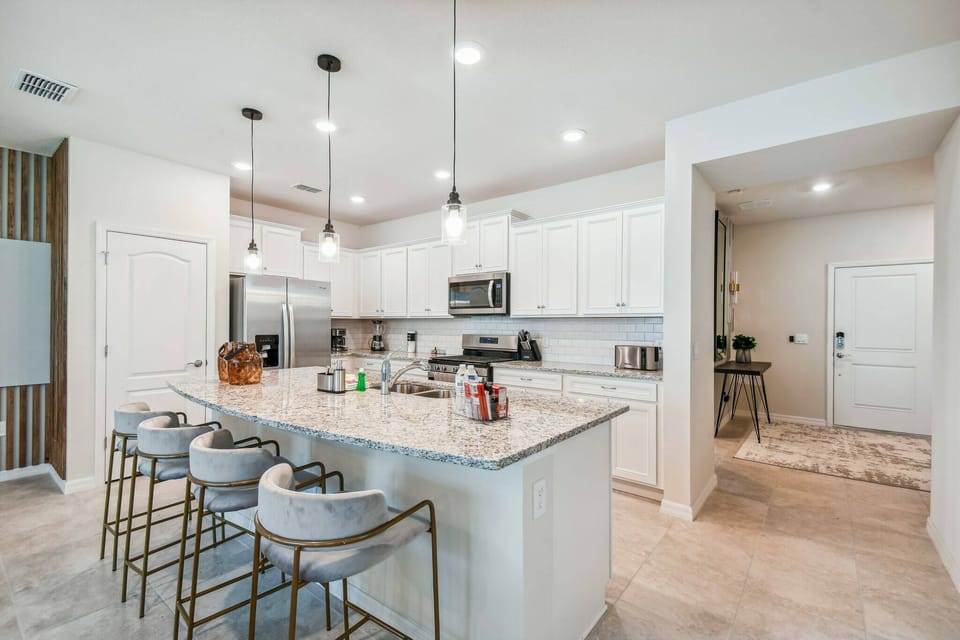 Explore a bright kitchen with chic white cabinetry and a gorgeous marble island, ideal for gatherings. The stylish bar stools enhance its elegance, while the open layout encourages smooth cooking and lively conversations.