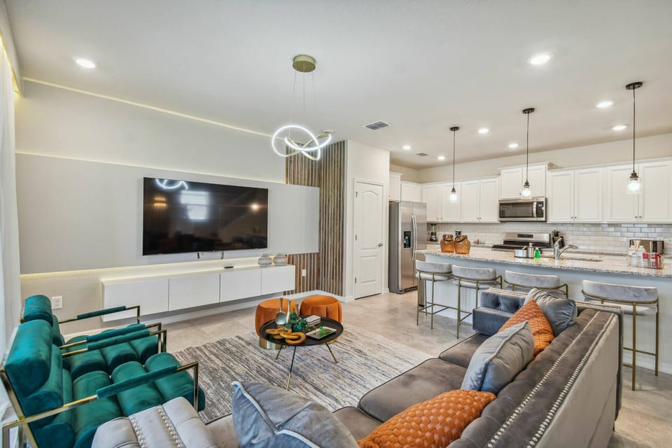 Enjoy the contemporary charm of this living area, where stylish teal armchairs and a plush gray sofa create a cozy space around a stunning coffee table, all beautifully illuminated by modern pendant lights.