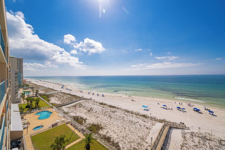 Sunlight dances across the calm coast as you watch families enjoy the inviting beach below