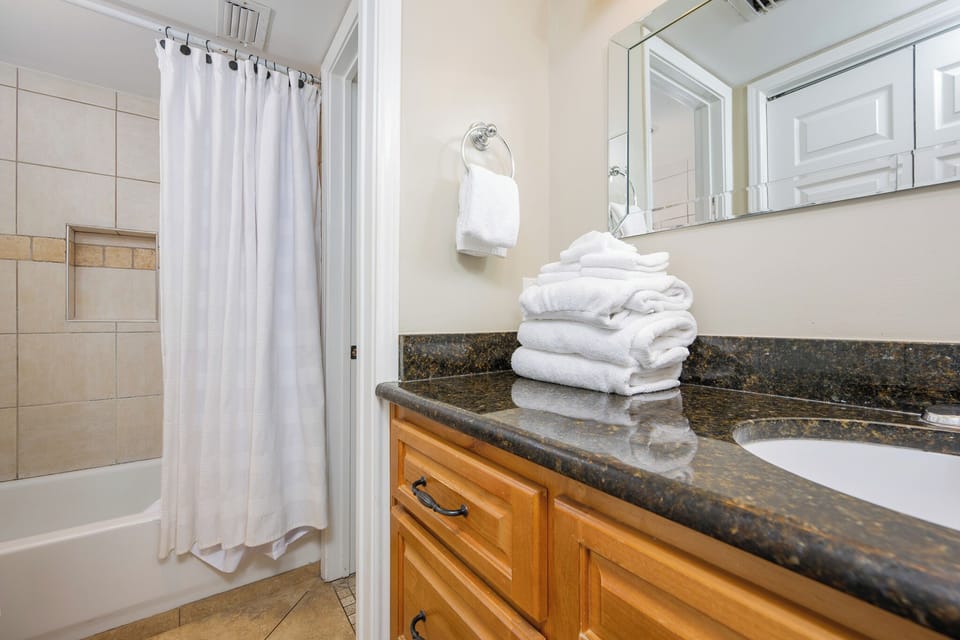 Soft white towels await in the master bath beside the polished granite countertop and shower curtain