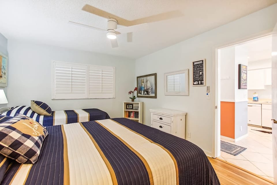 - Nautical charm fills this bedroom with a king size bed and twin for added flexibility
- Crisp striped linens, wood flooring, and fun art make it ideal for families or kids
- White shutters and ceiling fan create a fresh and breezy environment