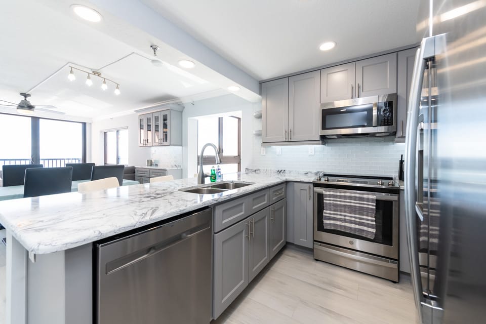 Fully updated kitchen with gray cabinets, stainless steel appliances, and a wide marble-style island.