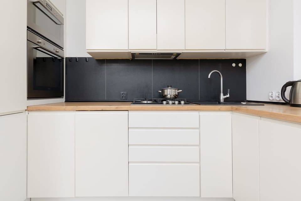 A sleek, fully equipped kitchen featuring white cabinets, a black backsplash, and all essential appliances for a convenient stay.

