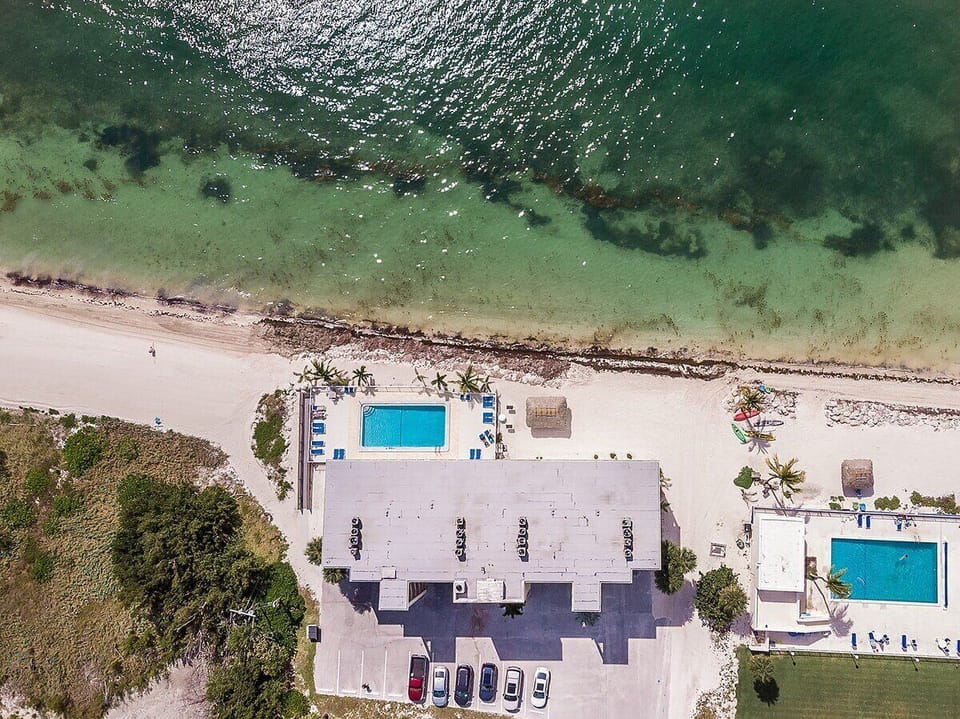 This aerial perspective highlights the property's oceanfront setting, community pools, private beach area, and direct access to the sparkling waters below.