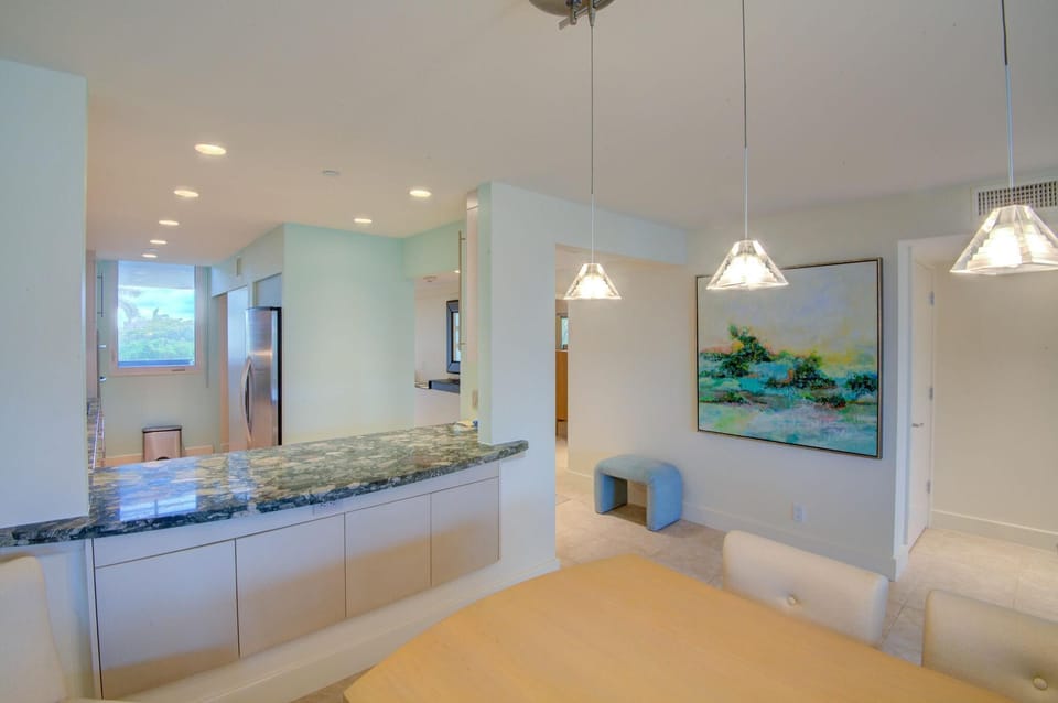 Green granite kitchen bar separates the dining area with pale wood table and beige upholstered chairs.