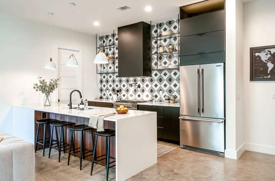 Cook together at the kitchen island with its gas range, pot filler faucet, and wine fridge; the black and white tile backsplash and pendant lighting turn dinner prep into part of the fun