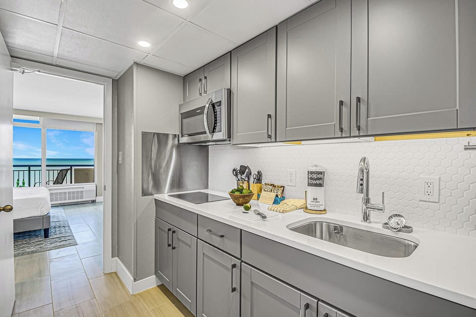 Modern kitchen with sleek cabinetry and a stylish blue-tile backsplash, fully equipped for your culinary needs. Just steps from the bedroom, this space offers convenience and functionality, allowing you to enjoy meals with a stunning ocean view.