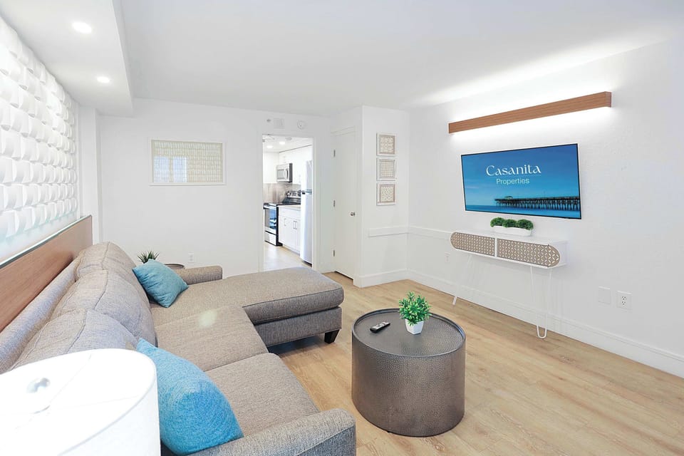 Relax in this inviting living space featuring a plush sectional sofa, wall-mounted TV, and modern decor. Perfect for unwinding after a day at the beach, this cozy area offers comfort and style, with easy access to the kitchen and bedroom.