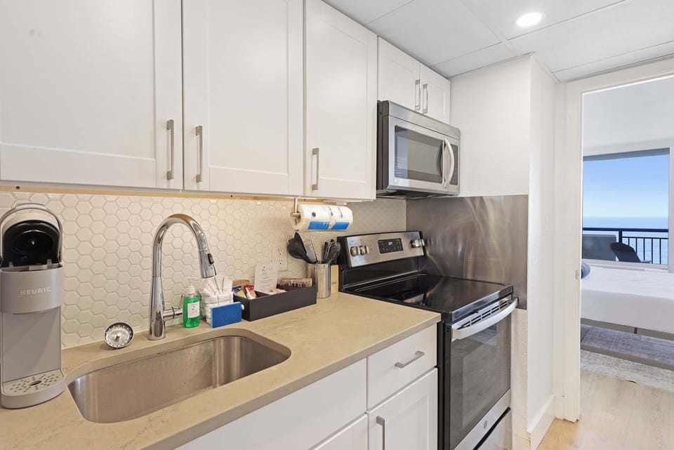 Modern kitchen with stainless steel appliances and ocean views from the bedroom beyond.