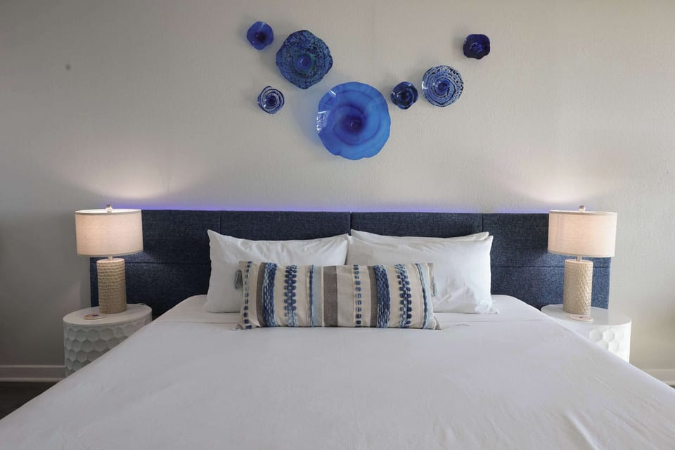 Wake up to beautiful beach views from this airy coastal retreat, featuring a plush bed, soothing blue décor, and a cozy seating nook by the balcony.