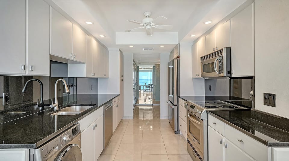 Glossy tiled floor leads through the kitchen, equipped with stacked washer and dryer, recessed lighting, and ceiling fan.