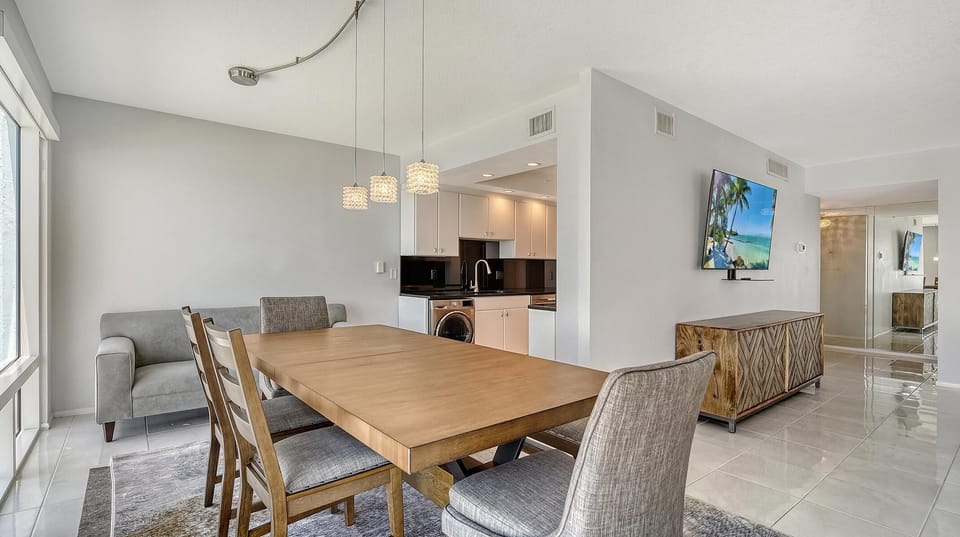 Wood dining table with mixed fabric and wooden chairs sits on a gray area rug by floor-to-ceiling windows.