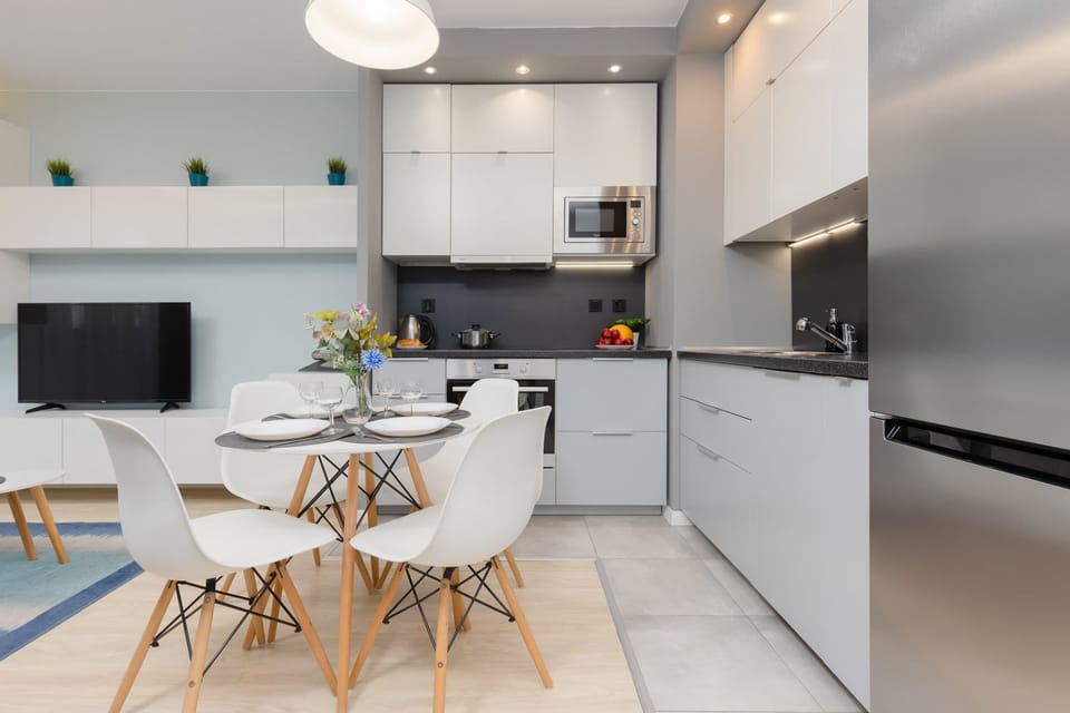 A modern open-plan kitchen and dining area with sleek white cabinetry, a dining table, and contemporary appliances.
