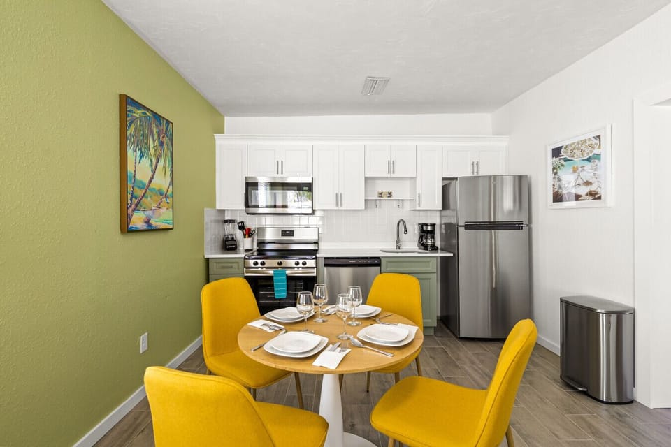 Siesta Key Beach kitchen and dining space with green cabinets, sunny yellow chairs, and palm-inspired art for a fresh, coastal vibe.