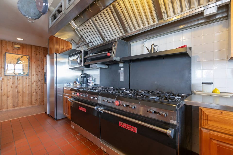 The massive commercial grade gas stovetop and double oven range and microwave oven in the kitchen.