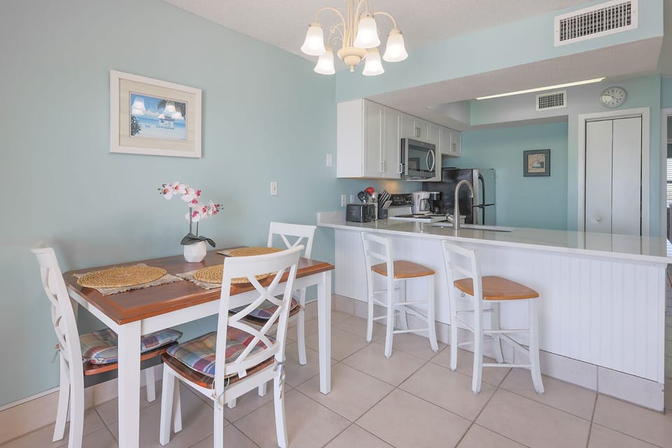 This bright kitchen features stainless appliances, granite countertops, and a cozy dining area with a charming beach view