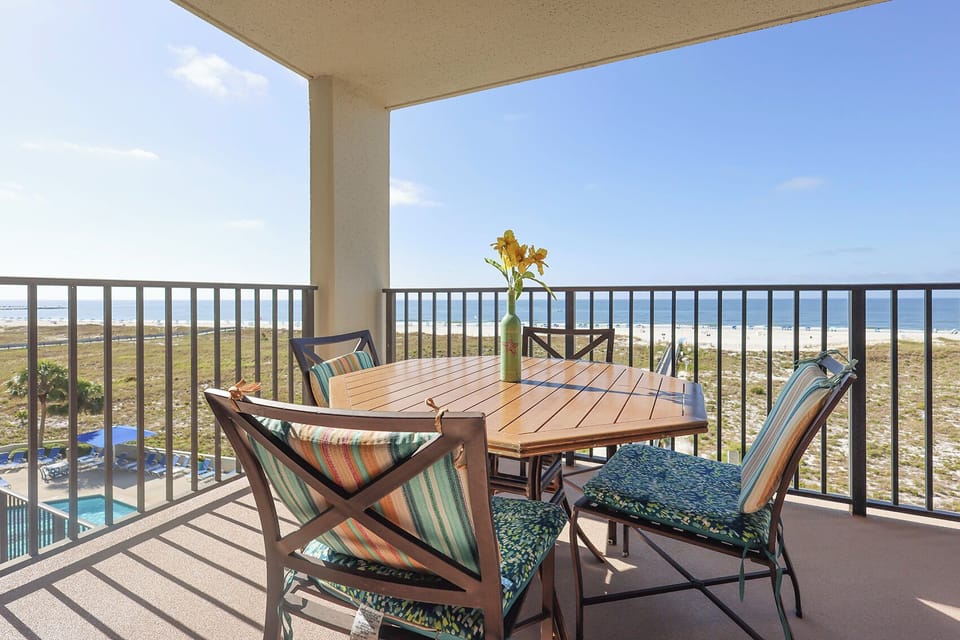 Balcony dining set with colorful cushions offers a serene view of the beach and pool area, perfect for relaxation