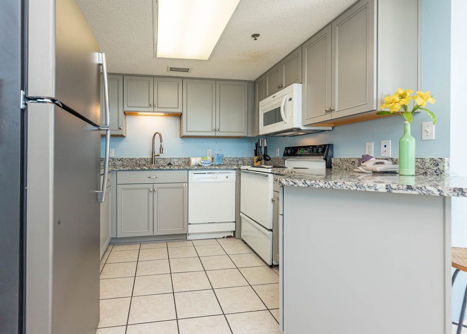 Kitchen features light gray cabinetry, granite countertops, and a breakfast bar with a view of the bright, inviting space