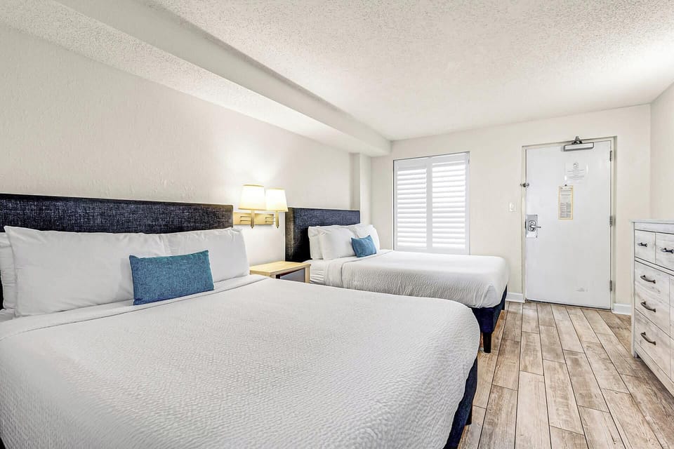 Rest easy in this bright, coastal-inspired bedroom featuring two plush queen beds, crisp linens, and calming tones—perfect for families or friends looking to unwind after a fun day at the beach.