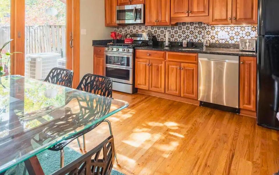 Enjoy meals in this stylish kitchen featuring stainless steel appliances, hardwood floors, and a spacious glass dining table.