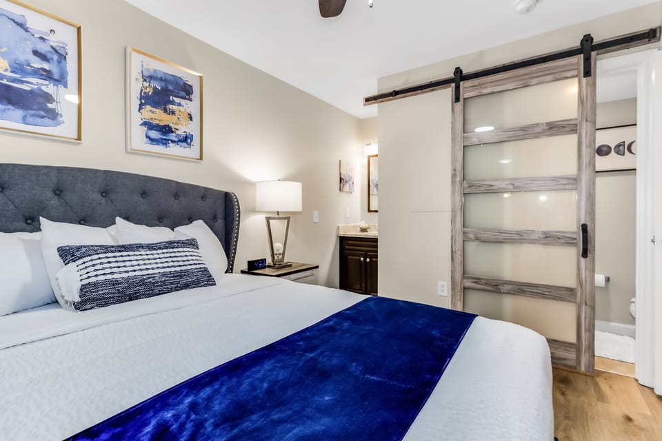 Sink into this plush bed with crisp linens and blue accents. The stylish barn door slides open to reveal your private ensuite bathroom—your peaceful retreat awaits.
