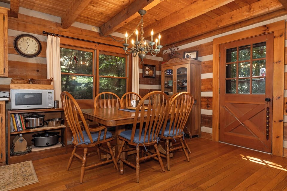 Gather around the rustic wood table beneath the warm chandelier glow, where cabin charm meets modern convenience. Sunlight streams through tree-framed windows, inviting you to linger over meals in this cozy retreat.