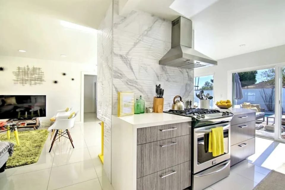 Bright kitchen with marble-slab backsplash, gas range, and sliding doors straight to the pool — indoor-outdoor flow at its best
