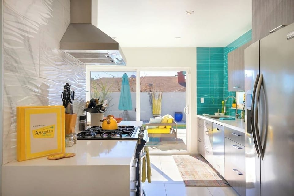 Sunlit kitchen with gas range, stainless steel fridge, turquoise tile backsplash, and sliding door to the backyard — breakfast with a pool view