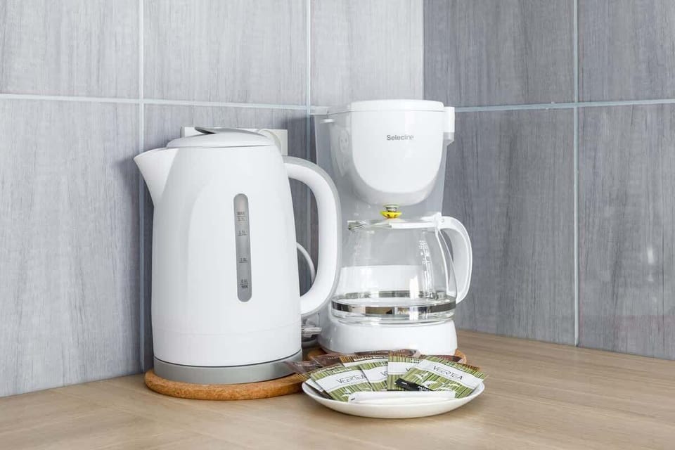A coffee and tea station with a kettle, coffee maker, and neatly arranged cups, ensuring guest convenience.
