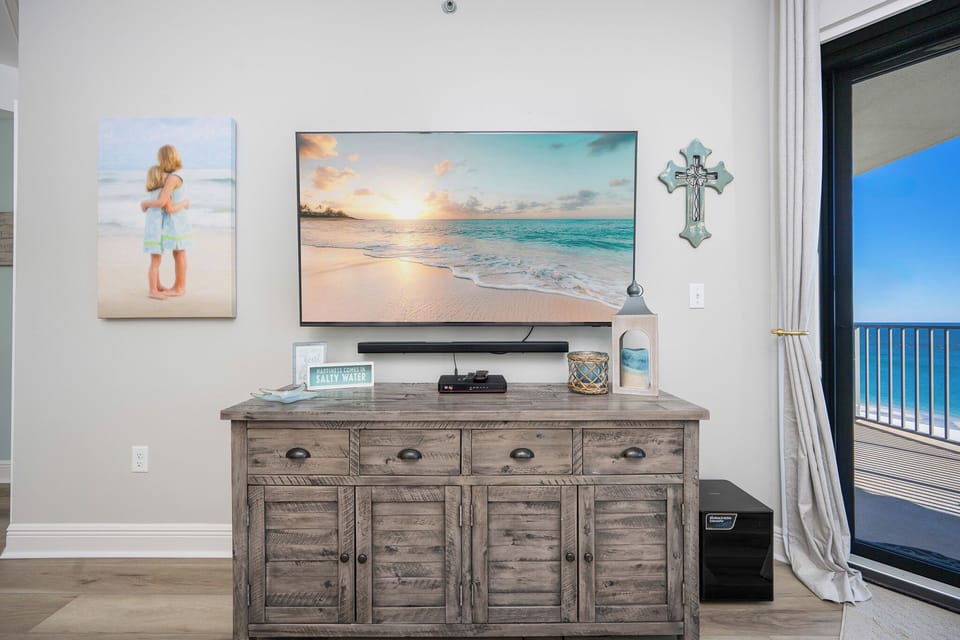 Coastal decor enhances the living area, featuring a TV, wooden cabinet, and access to a balcony with a view of the gulf