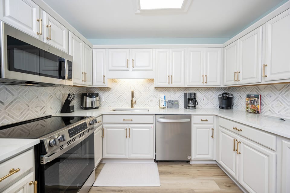 White cabinetry and elegant gold accents in this kitchen with a sleek countertop, Keurig, coffee maker, and backsplash