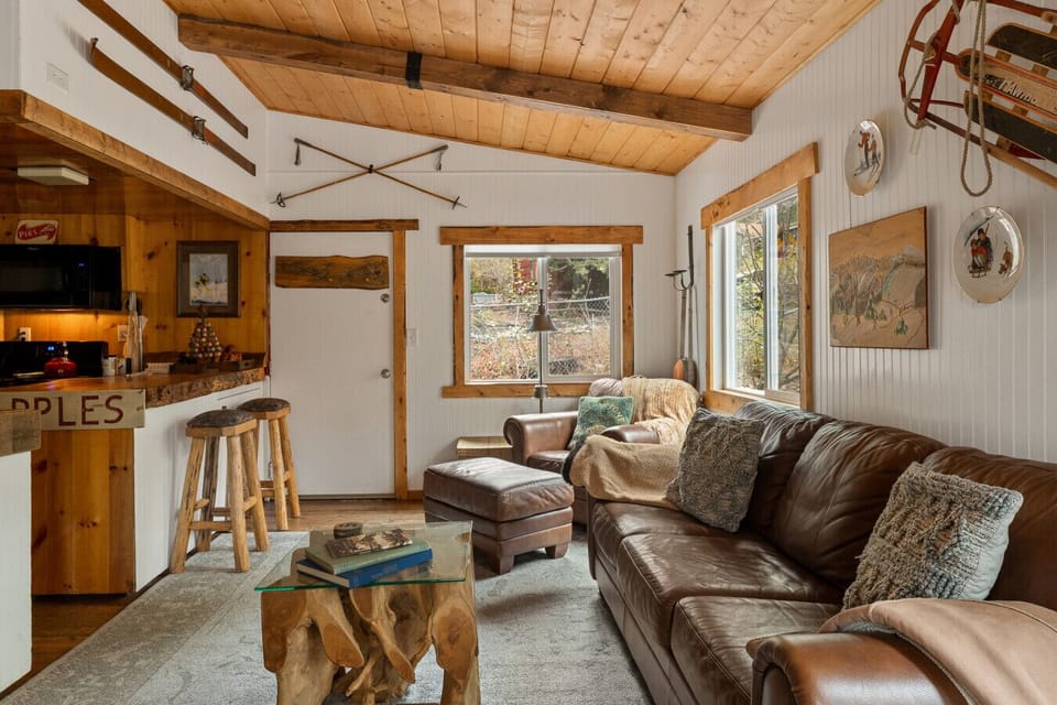 Relax in this charming rustic cabin living room featuring a comfy leather sofa, warm wood accents, and plenty of natural light — your perfect mountain escape!
