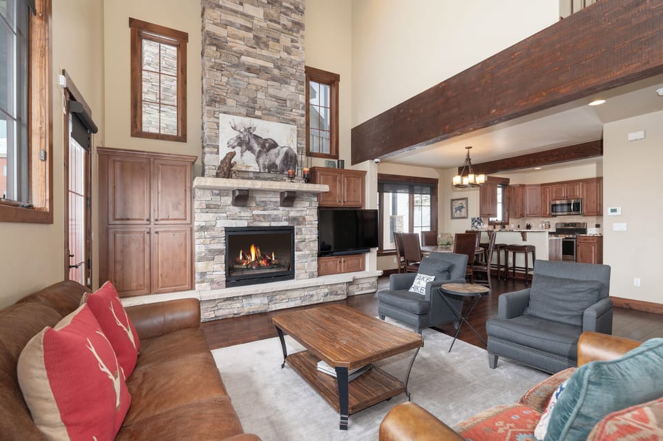 Gather around the crackling stone fireplace in this stunning open-concept space, where rustic beams and warm wood blend seamlessly with your mountain getaway comfort.