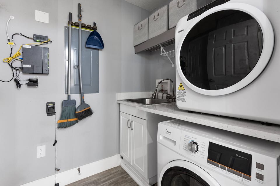 This laundry area boasts sleek white appliances against a calming gray backdrop, creating a tidy space for your essentials, while smart shelving ensures easy access to everything you need for a stress-free experience.
