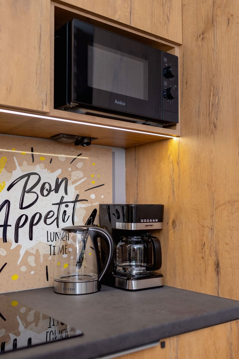 A close-up of the kitchen corner with a microwave, coffee maker, and charming "Bon Appetit" signage, offering convenience and charm.
