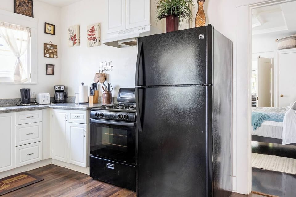 Gas stove, refrigerator, coffee maker, toaster, electric water heater, coffee bean grinder, french press, pots and pans below, full walk-in pantry (not shown in this view), doorway into bedroom.