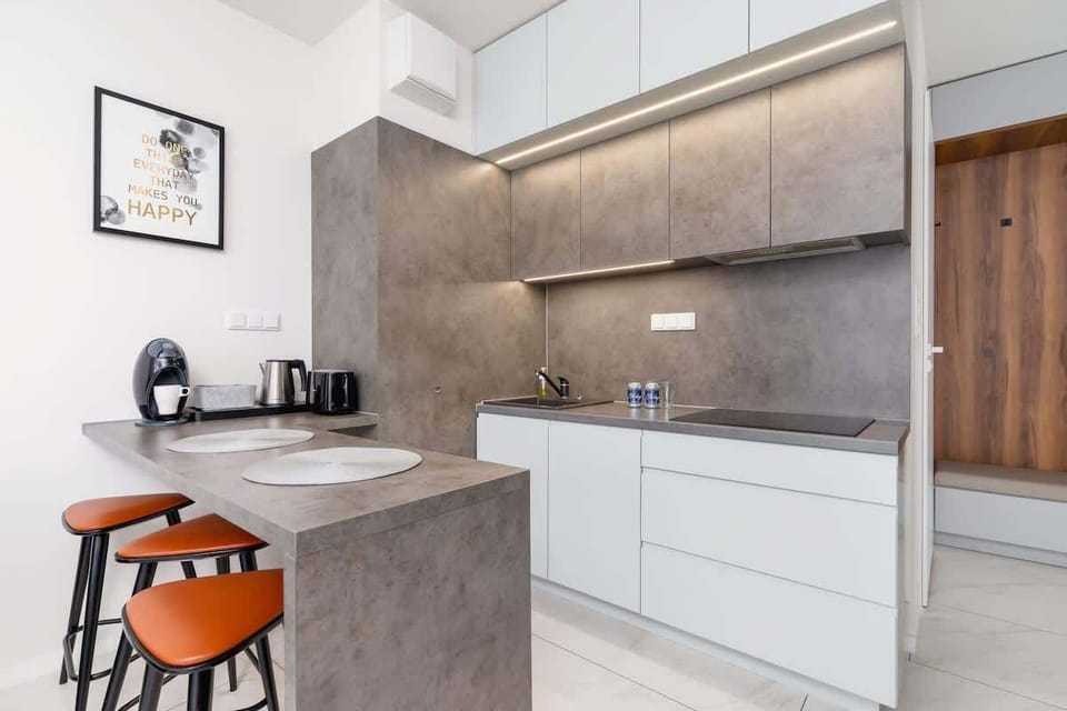 A compact kitchen with white cabinetry, concrete-style backsplash, and orange bar stools for a pop of color.
